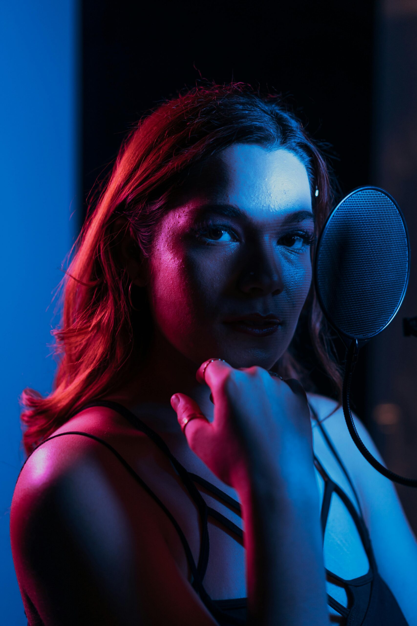 Moody portrait of a woman singer recording with colorful lighting in a studio.